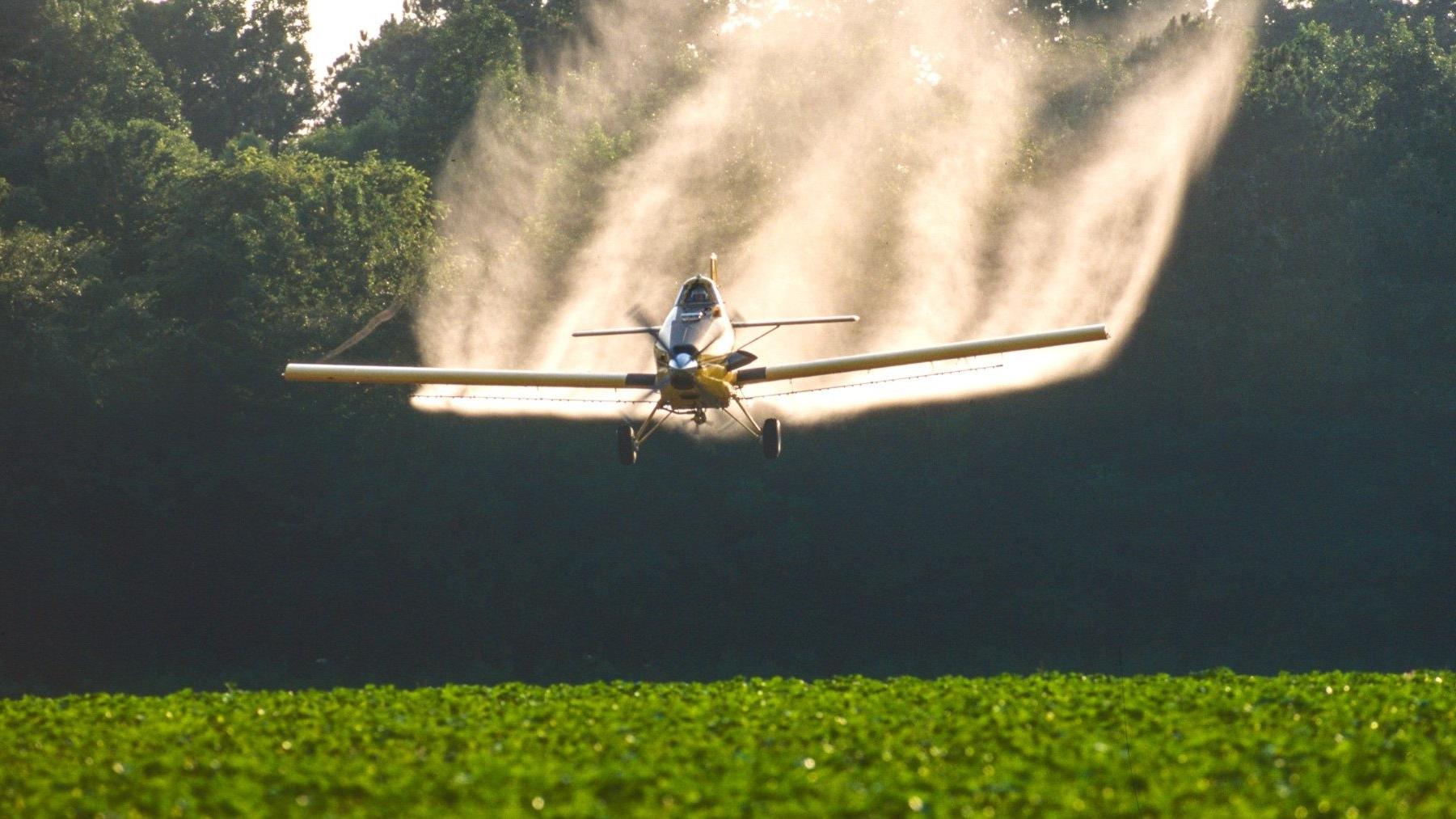 Crop duster plane spraying green field with chemicals.